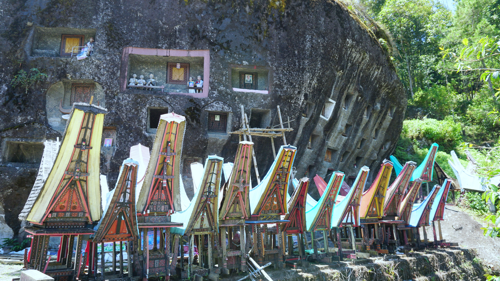 Colourful miniature tongkonans stand before a large rock with smaller burial chambers in Loko’mata. Photo by Upneet Kaur-Nagpal