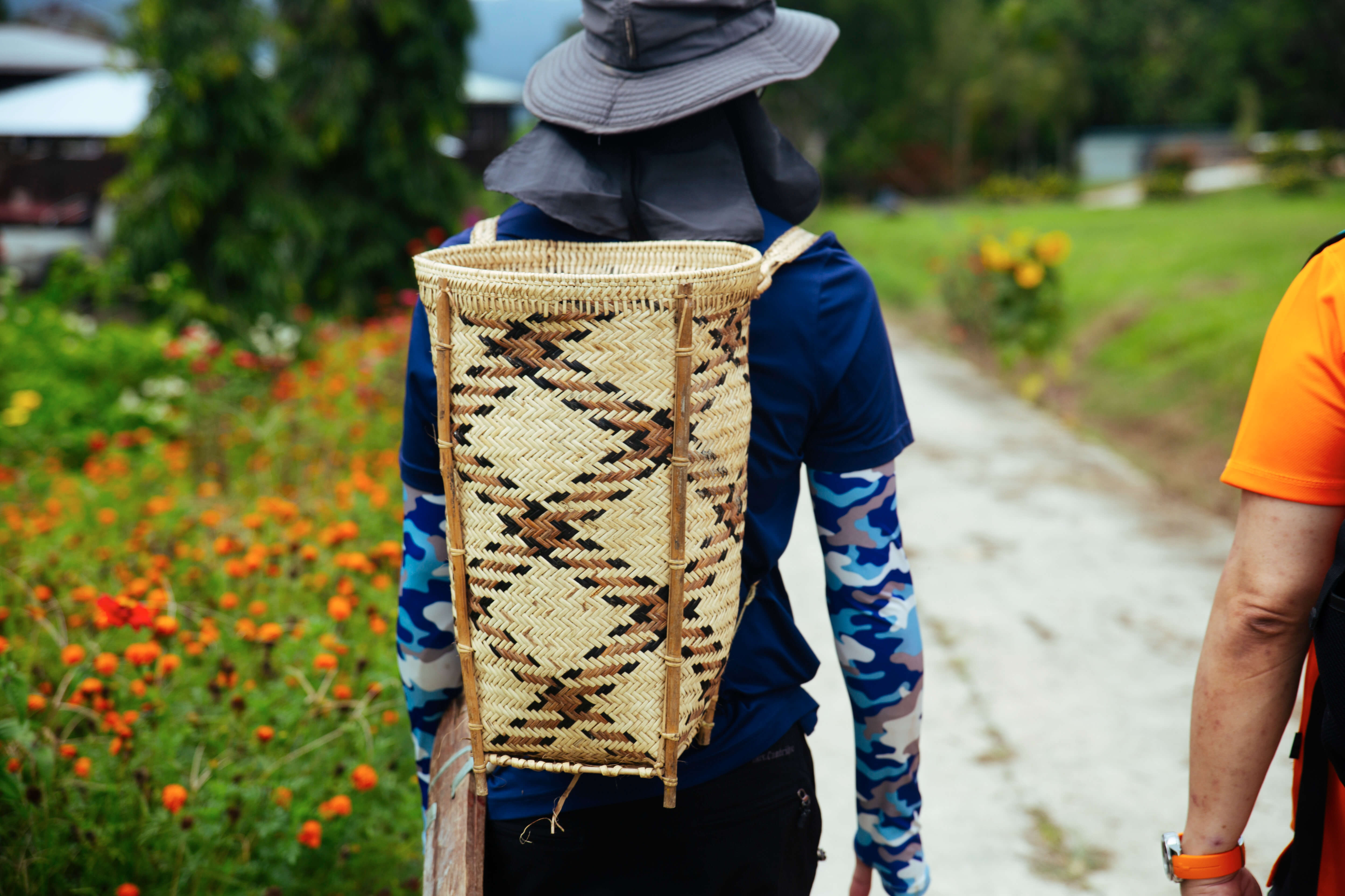 Back view of Zi carrying a basket woven with a criss-cross patten on his back. Farmers in Long Semadoh typically carry these hand-woven baskets called ren onto the fields 