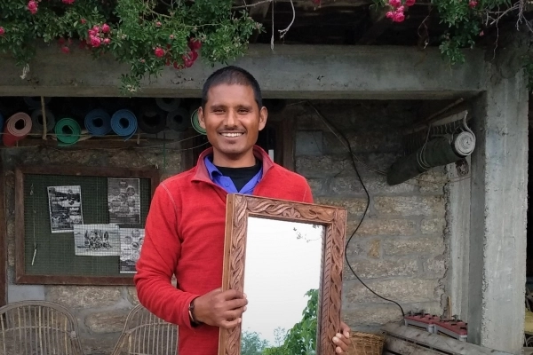 A man holds up a mirror with an elaborately carved wood frame