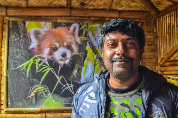 A man stands before a large photograph of a red panda