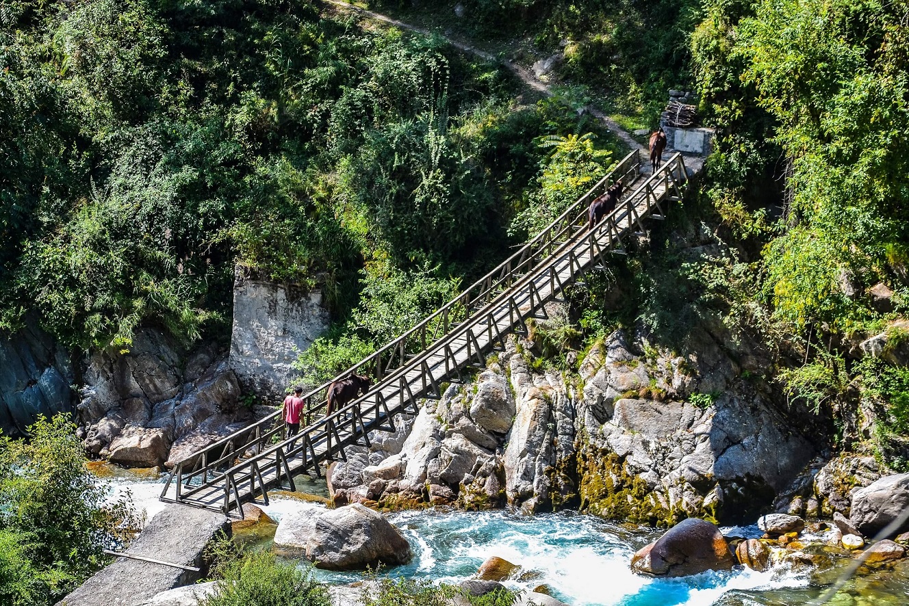 A man crossing a bridge over a river in a valley in the Himalayas, India