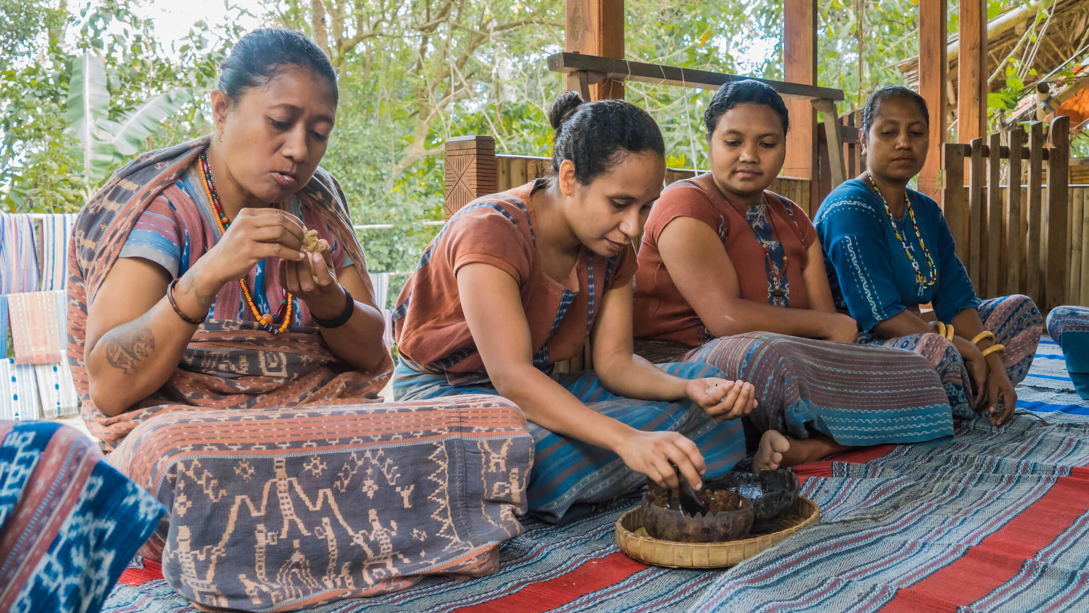 Rosvita (left), is seated alongside weavers Maria Nona Ice, Maria Suwanti, and Nona Eta, at the welcome ceremony. Guests eat rice and chicken heart, and drink chicken soup from a cup. Photo by Andra Fembriarto