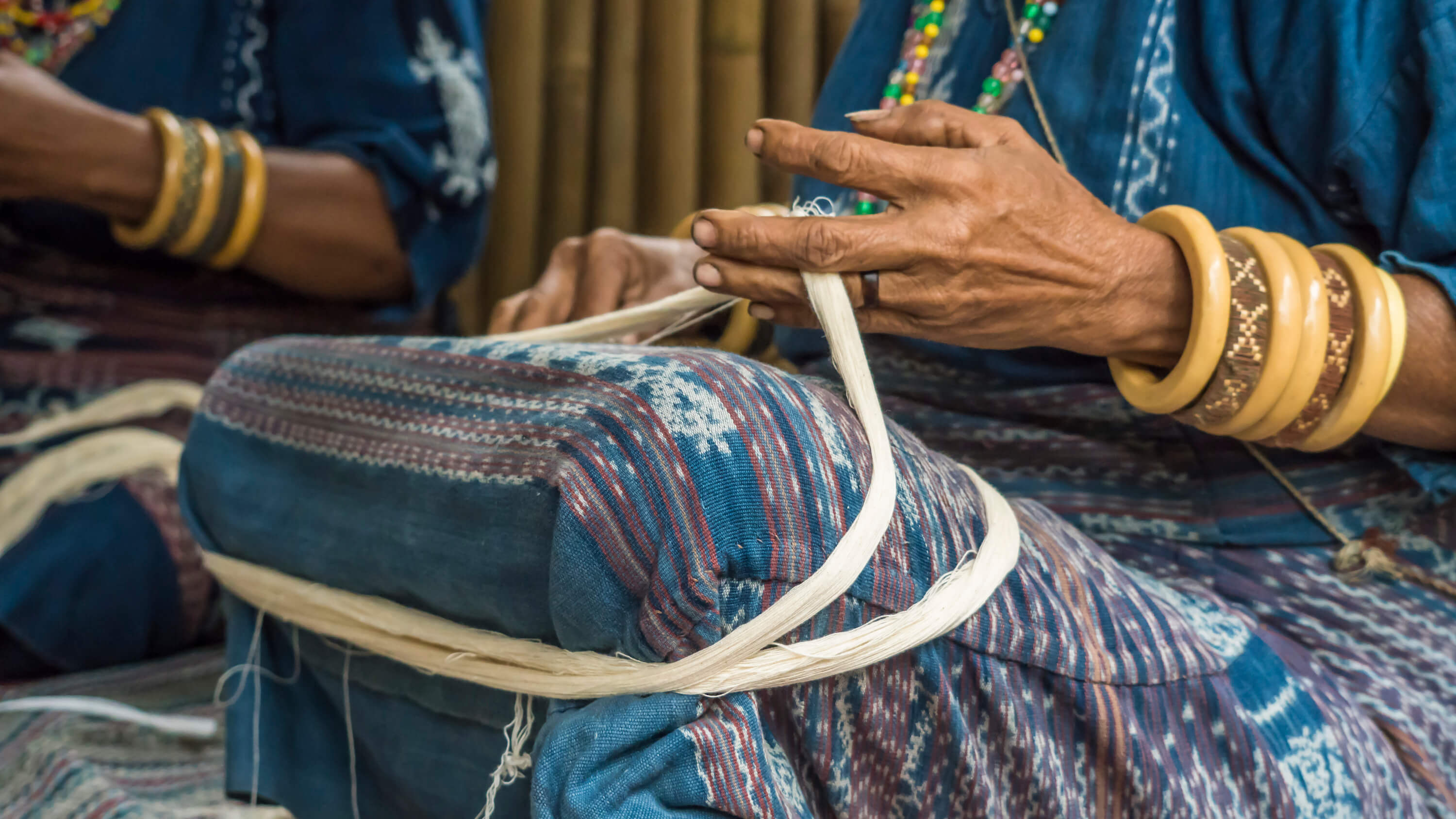 A Watubo weaver demonstrates how to ball up thread sans spinner, by rolling thread around her legs while seated. This is the first of many steps in the ikat weaving process guests get to learn about and try their hand at during the workshop. Photo by Andra Fembriarto 