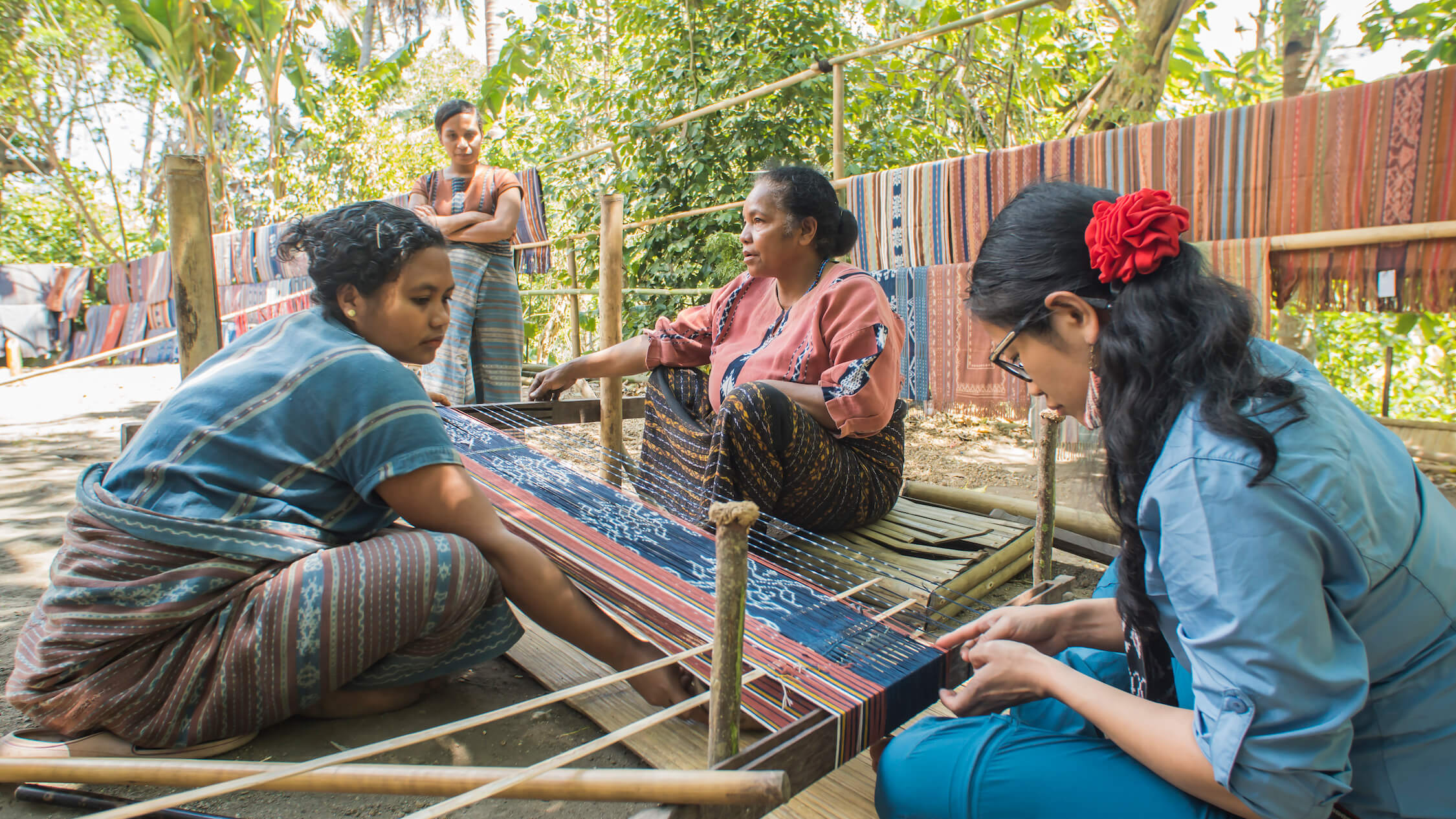Maria Suwanti instructs Grace on warping other coloured threads for striped detailing, using a local Watublapi motif set up for the lesson. Photo by Andra Fembriarto