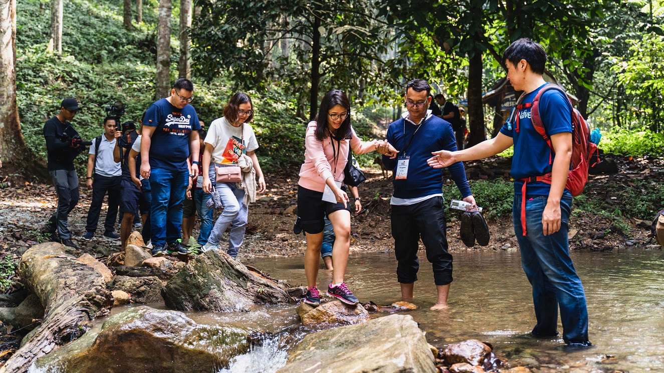 A group of hikers cross a stream in a forest in Malaysia.