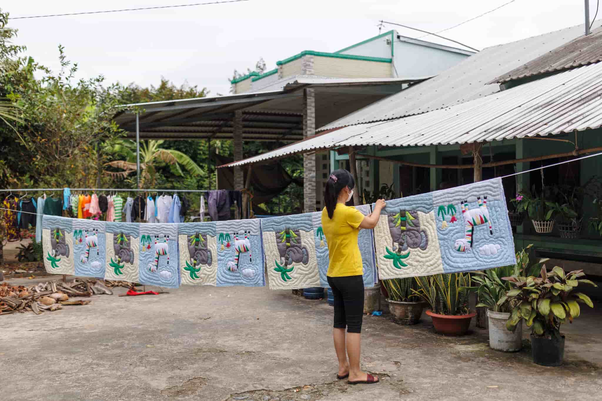A woman drying baby quilts in a yard. 