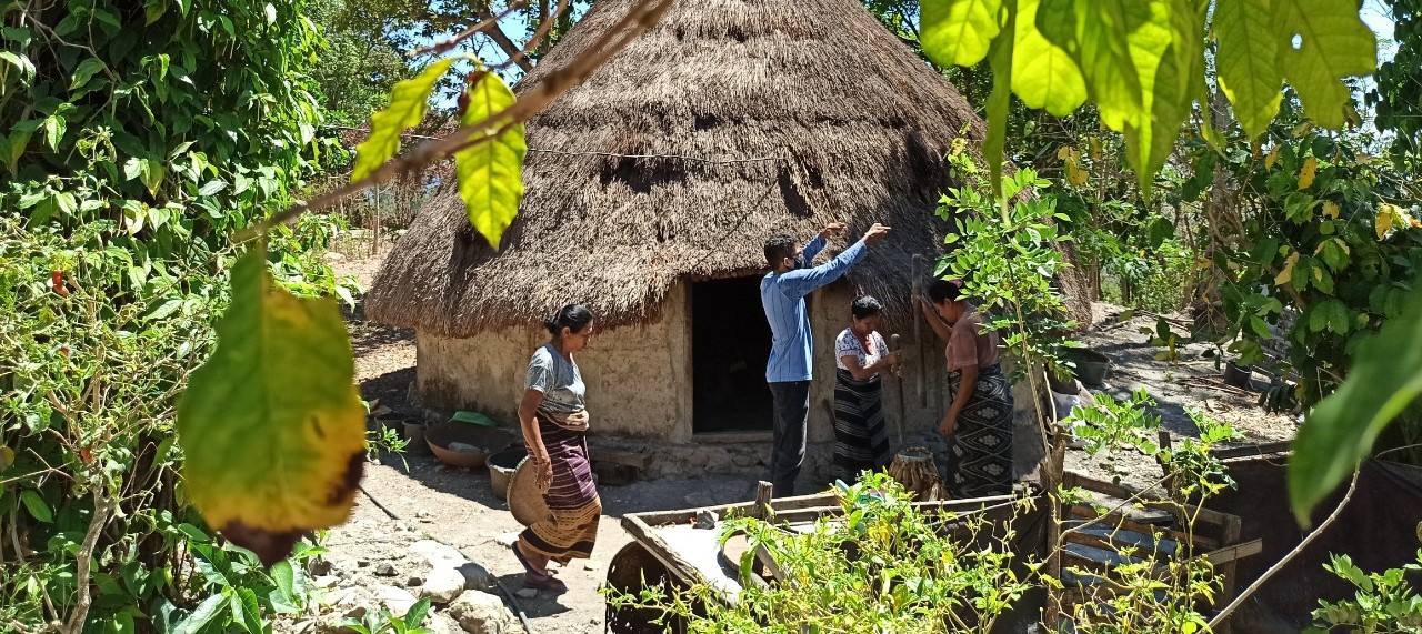 Two women and a man stand before a house with thatched roof in Mollo, Indonesia