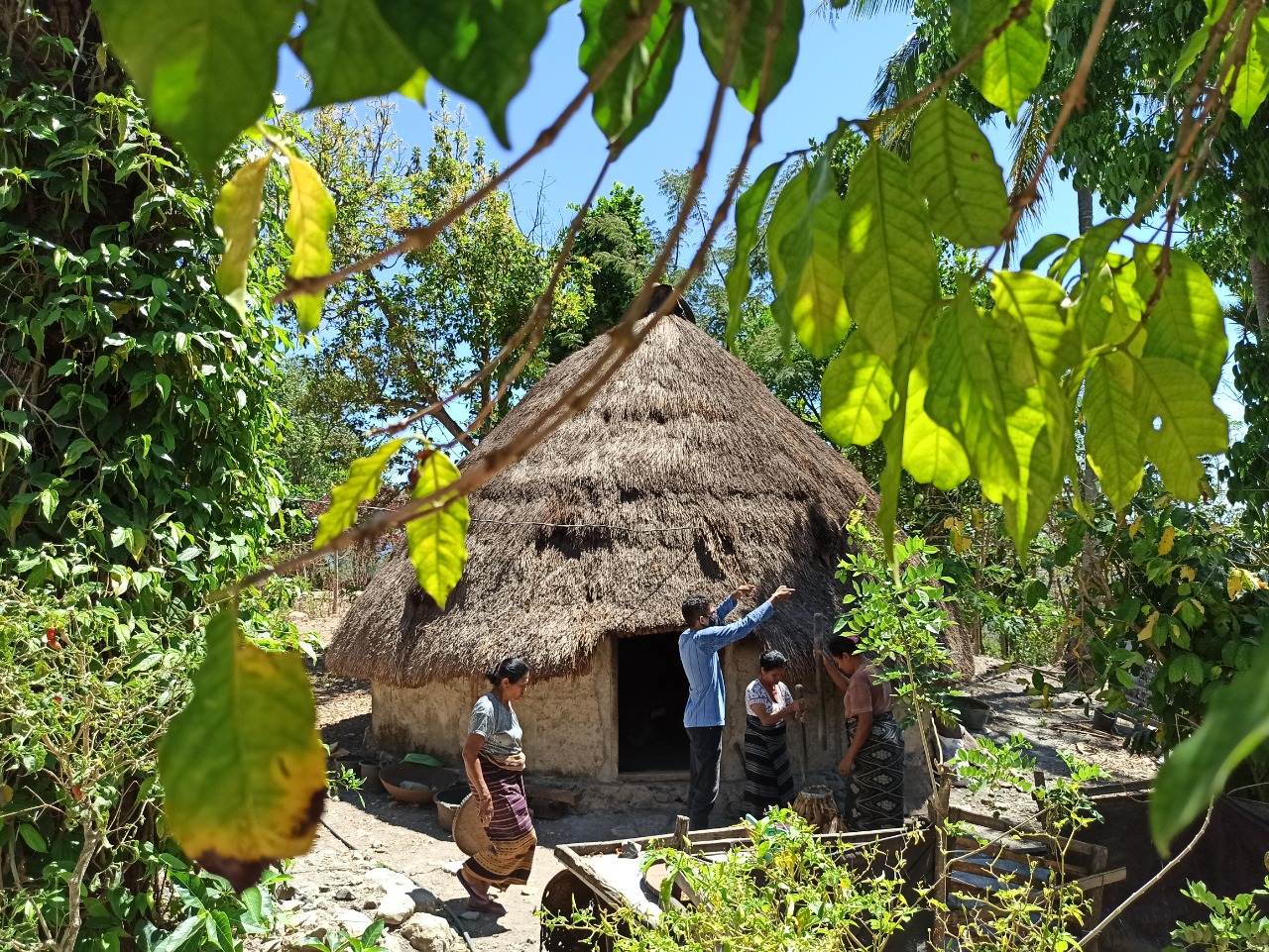 Two women and a man stand before a house with thatched roof in Mollo, Indonesia