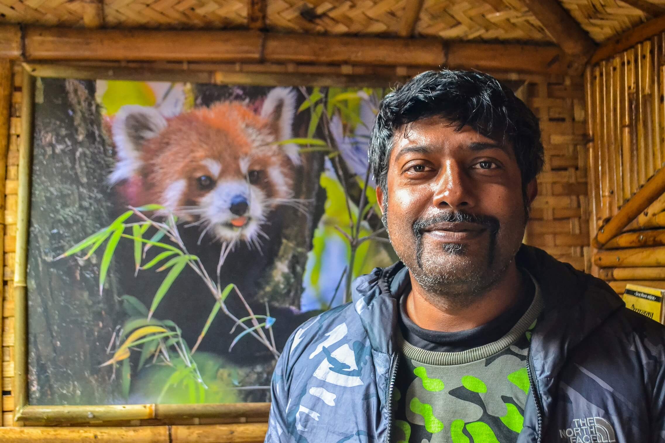 A man stands in the foreground with a photo of a red panda in the background