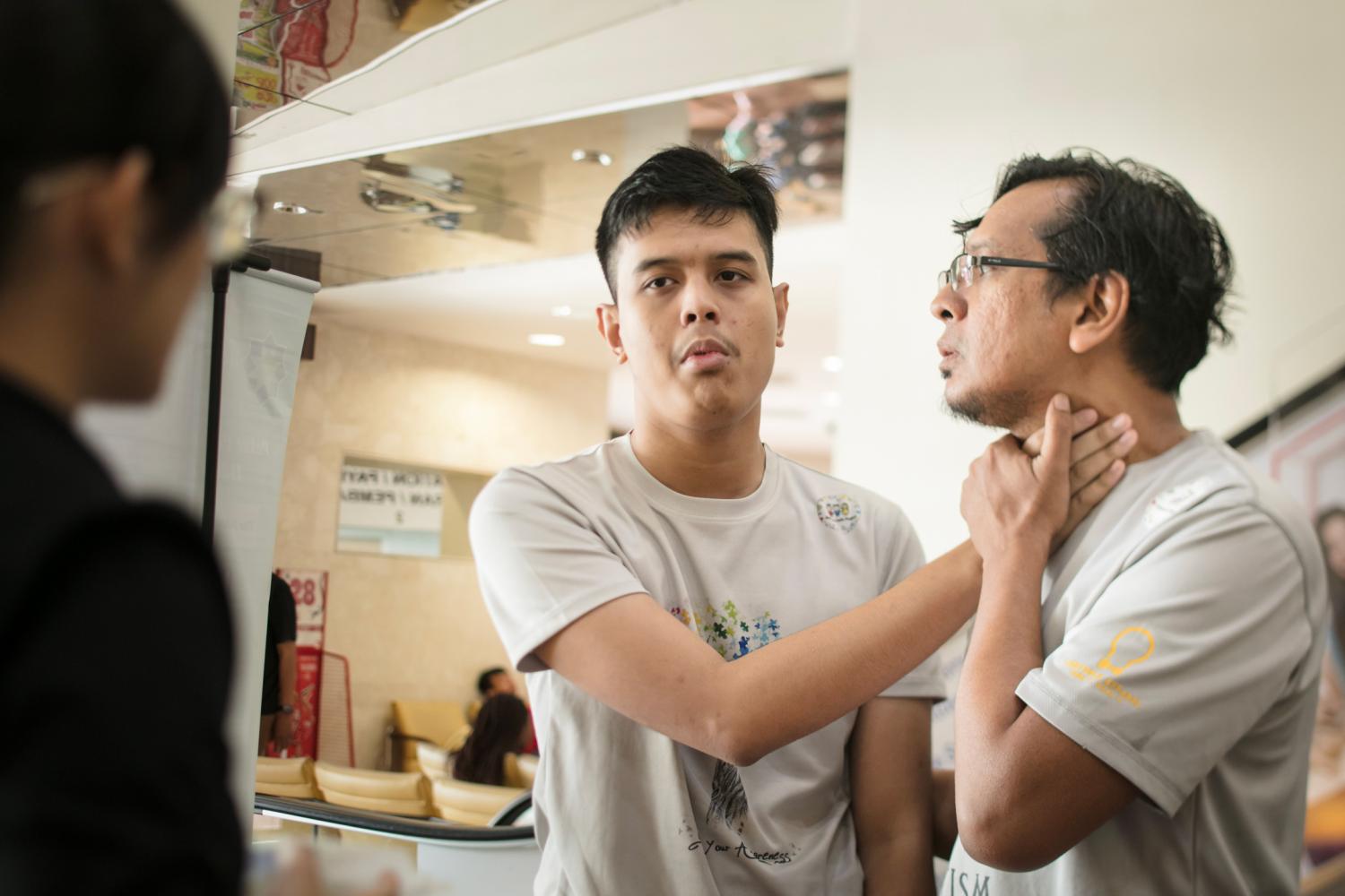 When talking to customers, Adli helps Luqman regulate the volume of his voice by letting him feel the vibration from his vocal chords. When talking to customers, Adli helps Luqman regulate the volume of his voice by letting him feel the vibration from his vocal chords.