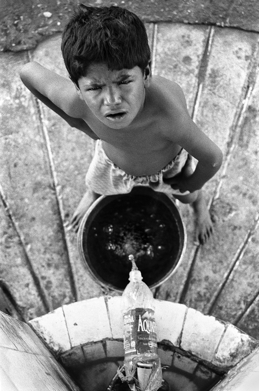 WATER FROM A BOTTLE: A young rag-picker takes a break from sifting through refuse and collects water for his bath WATER FROM A BOTTLE: A young rag-picker takes a break from sifting through refuse and collects water for his bath