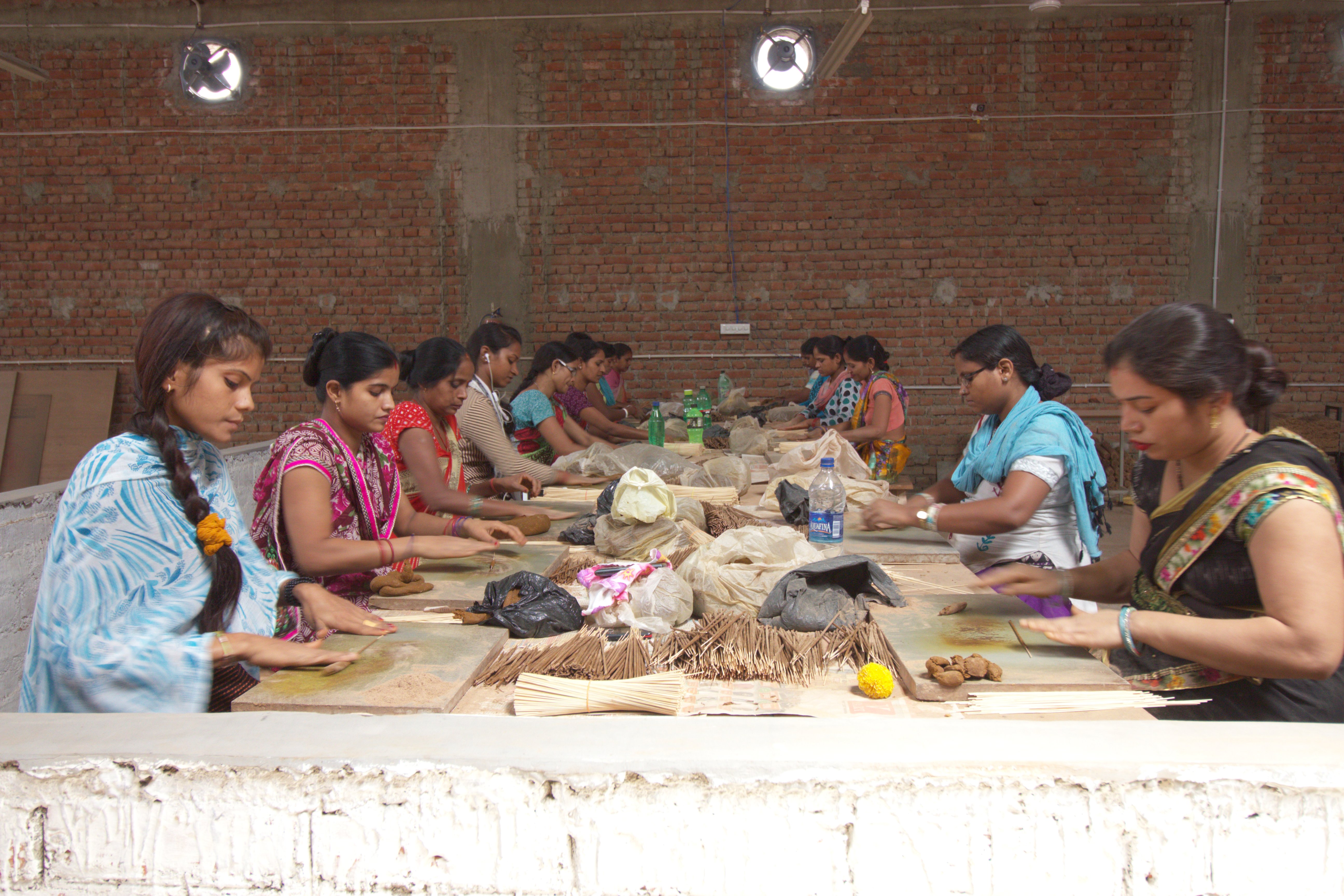 Women sitting around a table making incense sticks with their hands