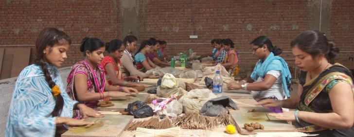 Women sitting around a table making incense sticks with their hands