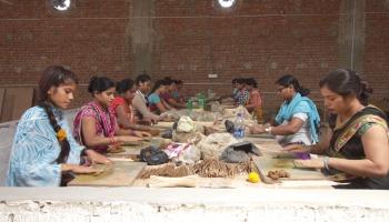 Women sitting around a table making incense sticks with their hands