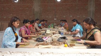 Women sitting around a table making incense sticks with their hands