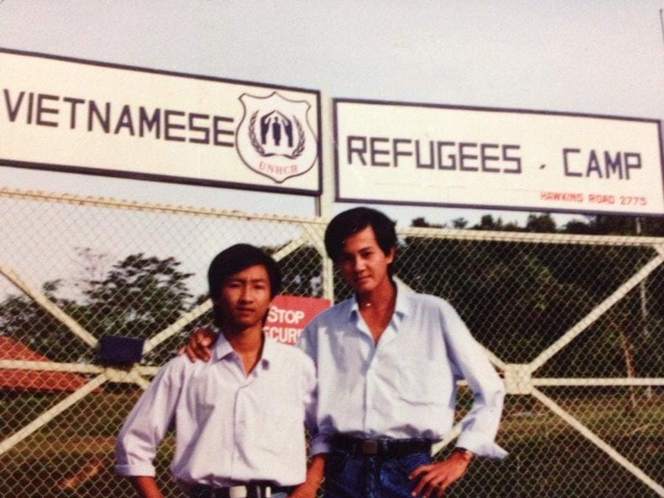 Two men stand before a gate bearing the sign Vietnamese Refugees Camp, in Singapore, which once accepted refugees in the 1970s. 