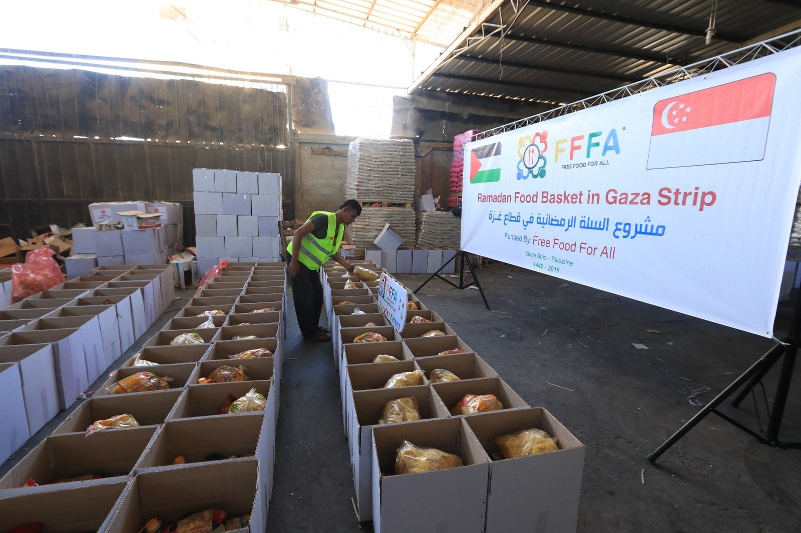 A man checks the food items neatly packed in rows of boxes sit in a warehouse, before they are shipped to families in need on the Gaza Strip