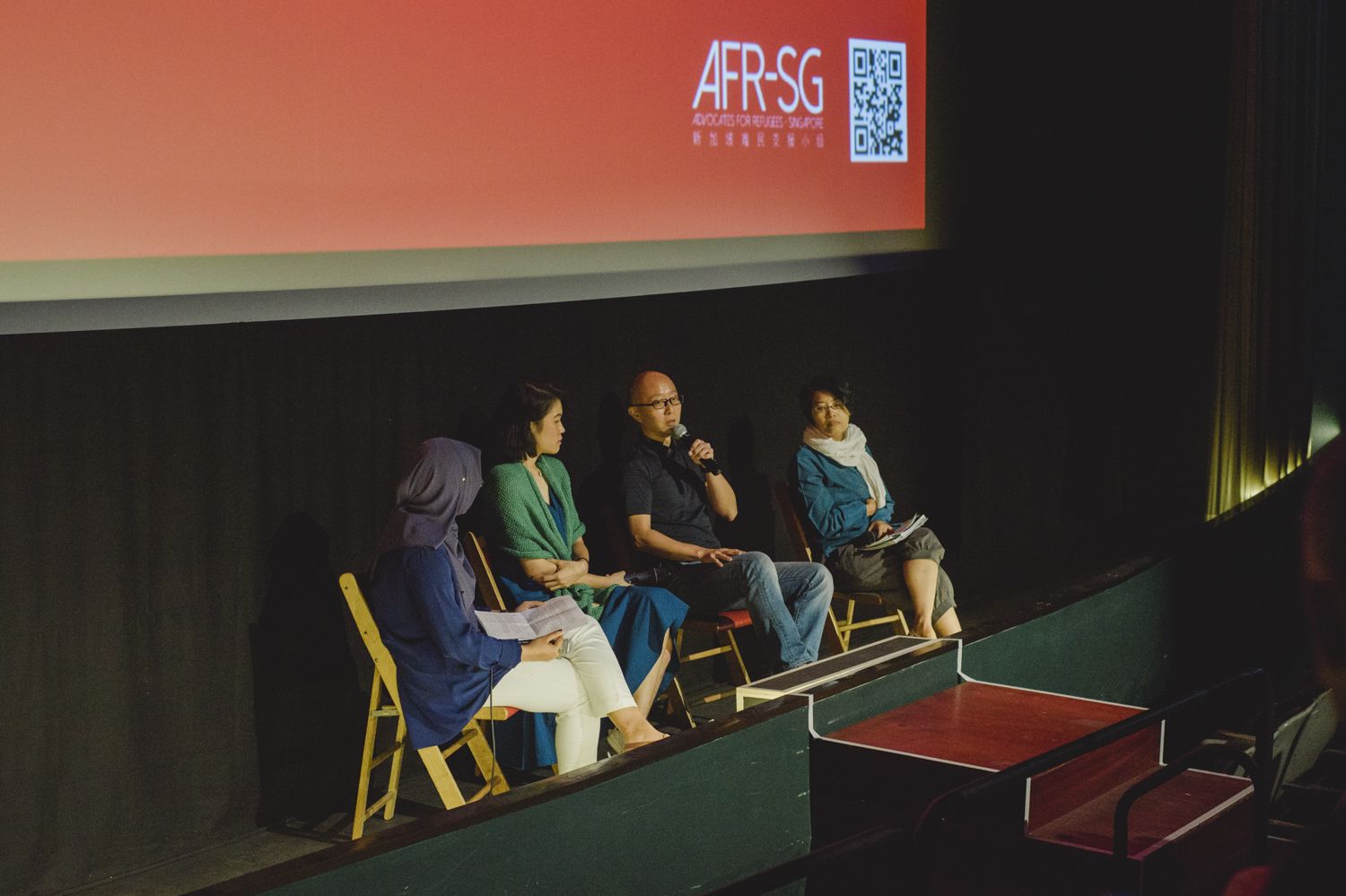 Four panellists sit onstage at a talk organised by AFR-SG to promote awareness of issues surrounding refugees.