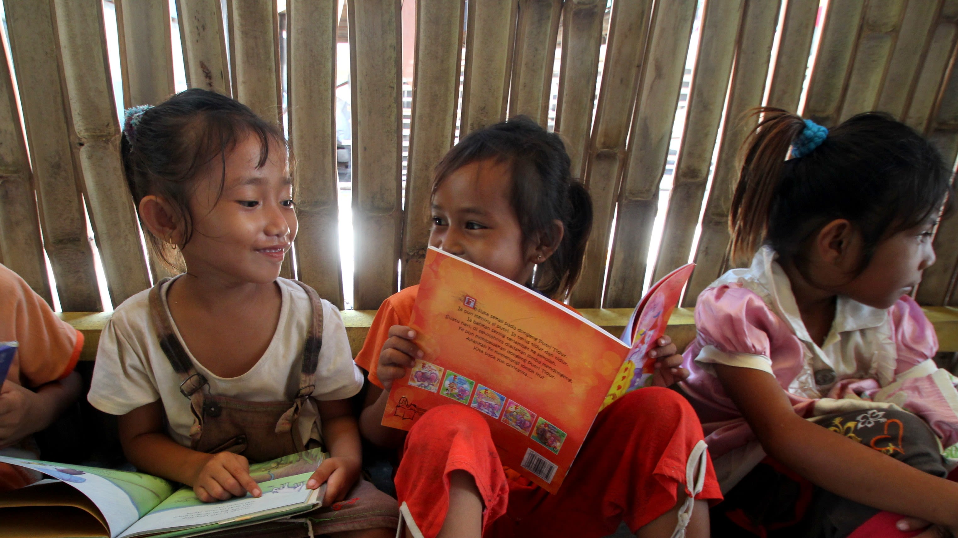 A group of girls sit on the floor reading a book in a library