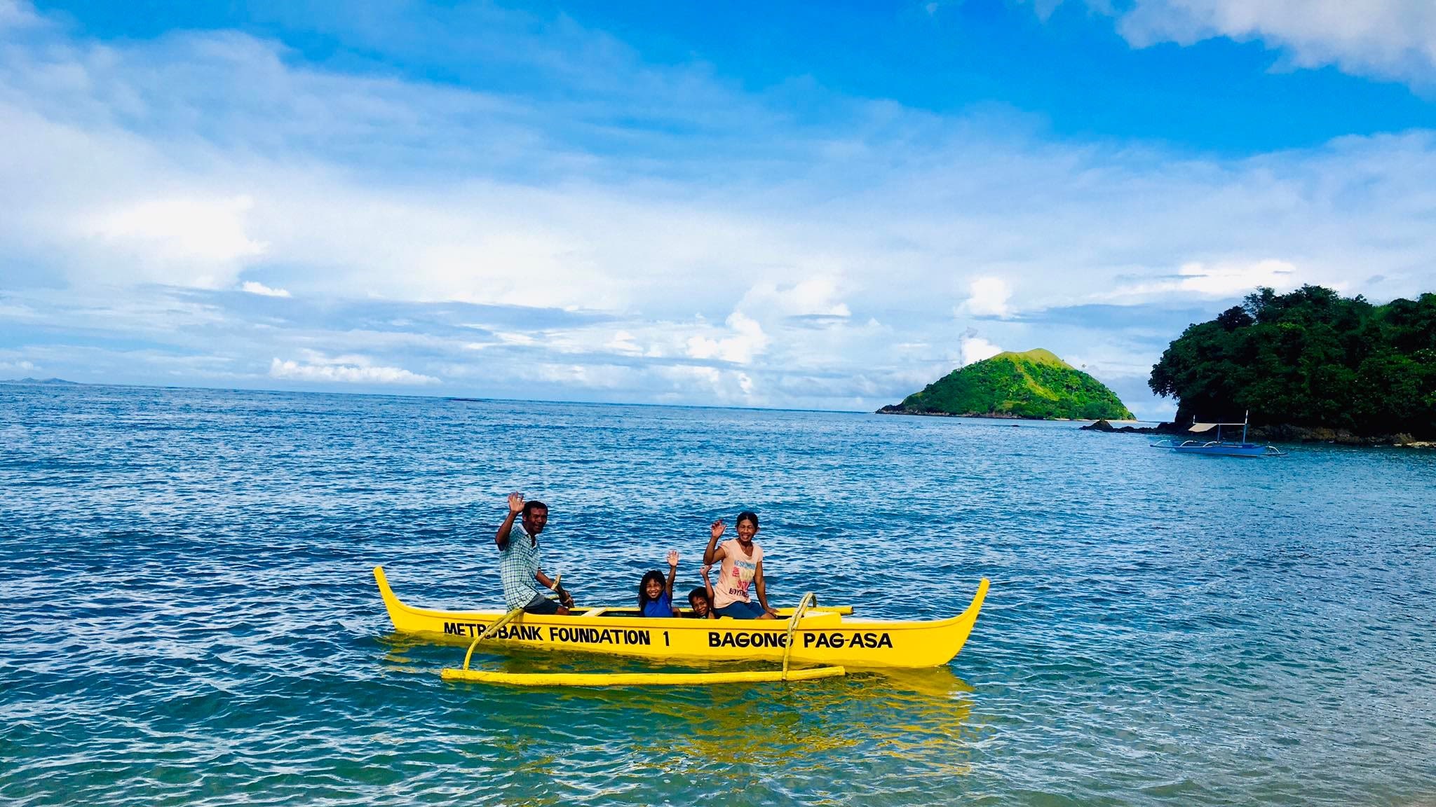 A man and woman on a yellow boat with their two children, by the beach in the Philippines. 
